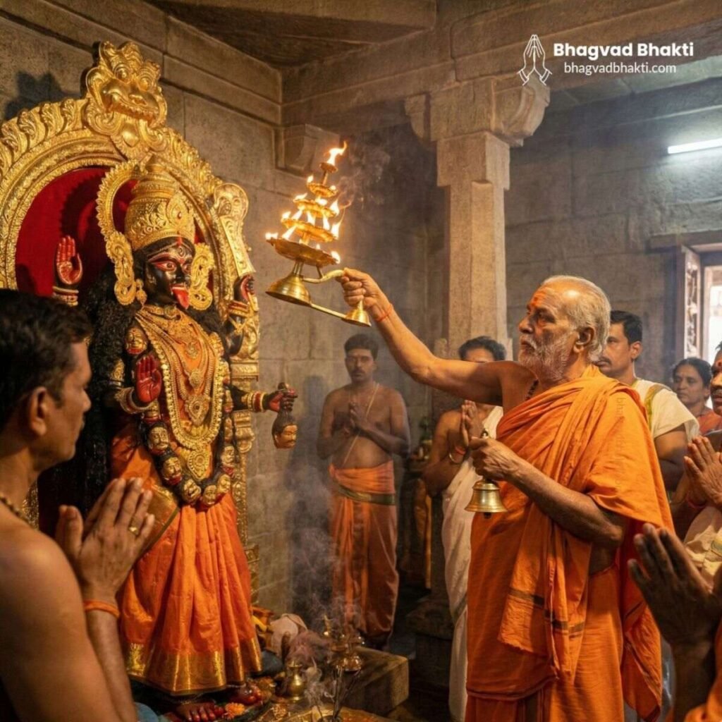 पत्थर के मंदिर के गर्भगृह में काली माता की काली-मुखी मूर्ति के समक्ष वरिष्ठ पुजारी आरती (mangal ki seva sun meri deva lyrics) कर रहे हैं
